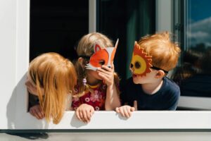 3 Kinder mit Tiermasken stehen lachend am Fenster